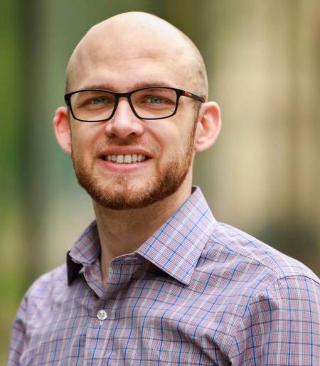 Picture of Nils Deppe sitting and smiling with a blurred background.